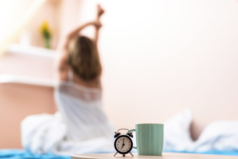 Blurry image of a woman waking up, with an alarm clock and a mug in front.